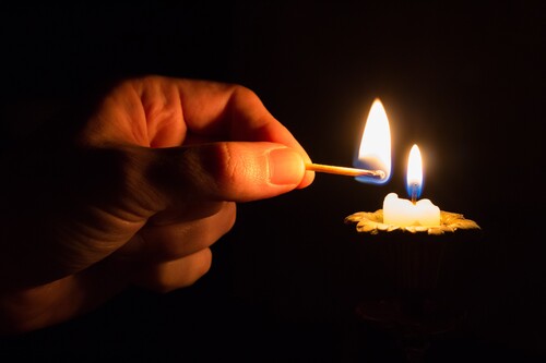 person-holding-match-stick-with-fire-in-front-of-candle-with-fire.jpg